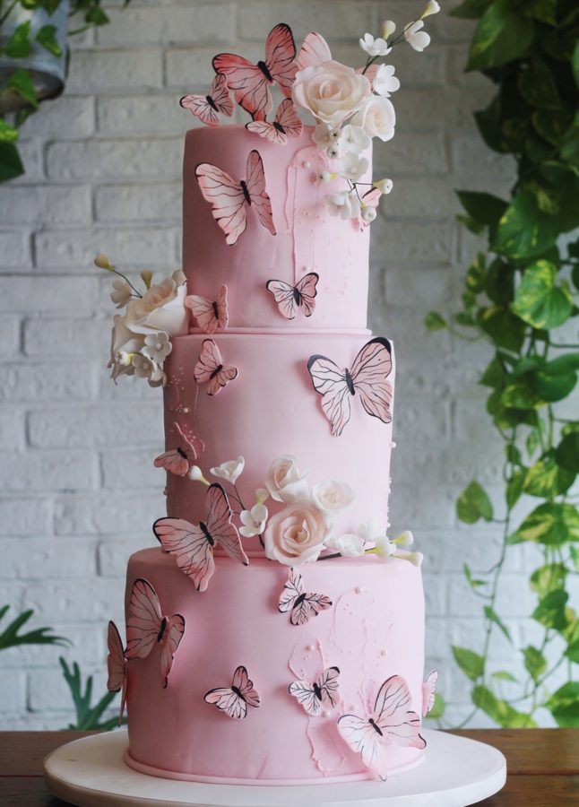 Pastel de tres pisos rosa decorado con mariposas y flores